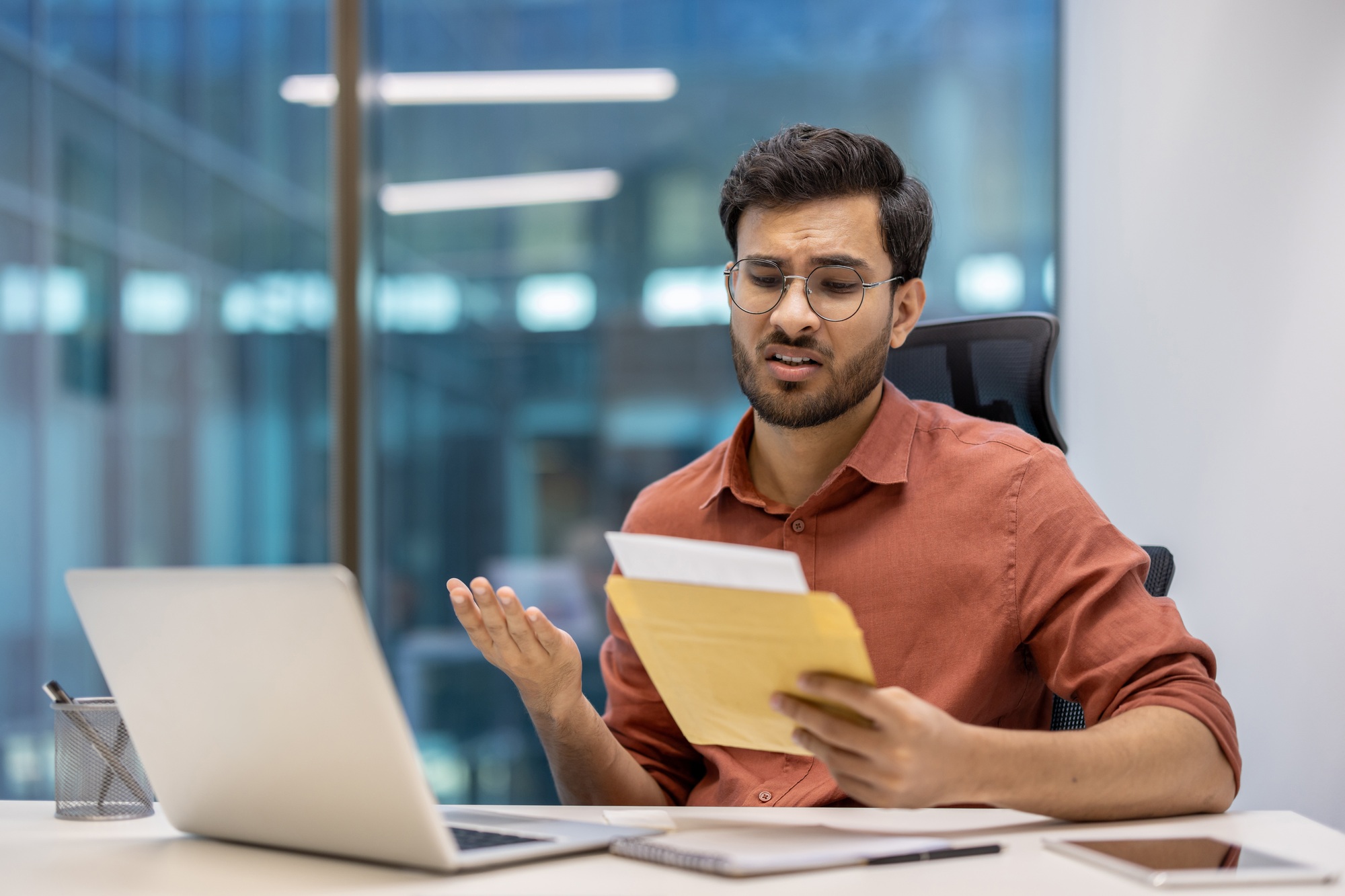 Young professional in office looks concerned after receiving bad news in postal envelope